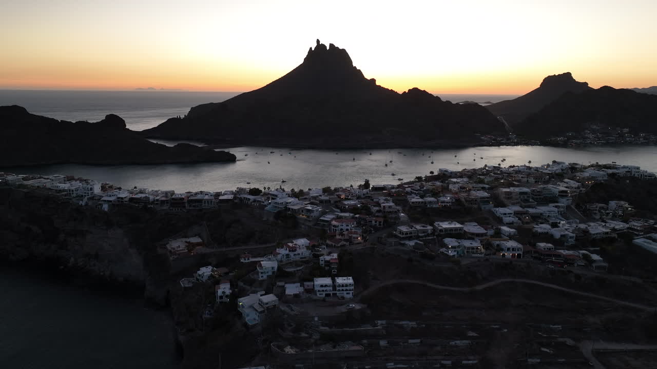 Ascending aerial shot of a small town with mountains and sea with sailboats at dusk