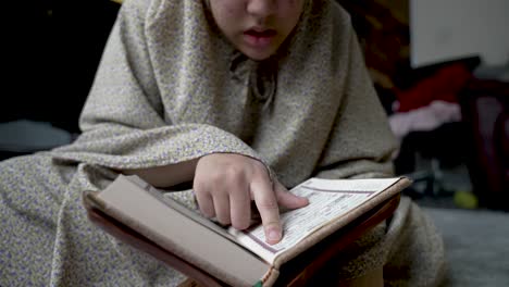 joven musulmana sentada en el suelo cubierta por ropa de hijab, leyendo un libro religioso con el dedo, encarnando el concepto de estudiar y aprender en casa