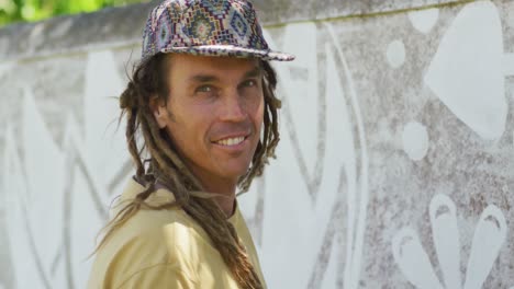 video portrait of smiling caucasian male artist with dreadlocks painting mural on wall