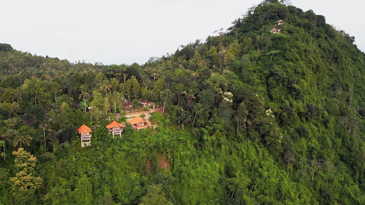 Tropical hillside retreat in Bali Sidemen perched on steep green mountains surrounded by dense forest and lush vegetation with dramatic elevation and depth wide angle drone view