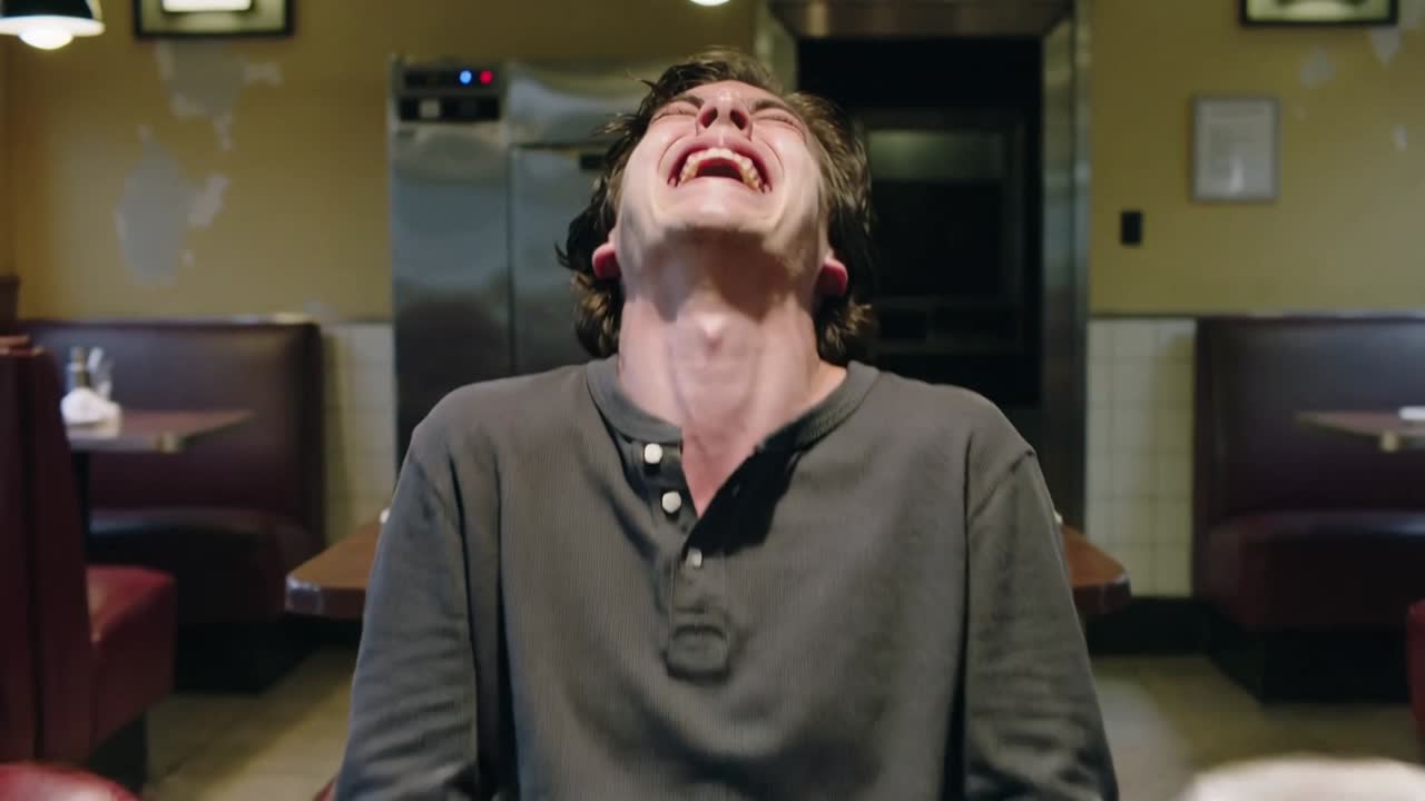 Reacting adult male in dark grey henley holding head back at diner booth, with cluttered mugs