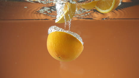 Cámara-Lenta-De-Naranjas-Frescas-En-Rodajas-Cayendo-Al-Agua-Sobre-Fondo-Naranja