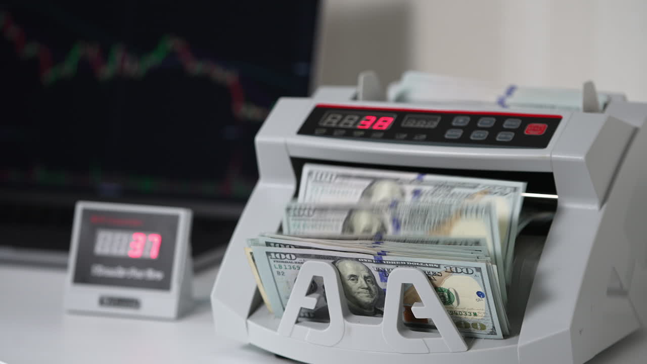 Male hand puts a wad of money into counting machine. Electronic money cash machine counting one hundred dollar bills. Close up. Blurred backdrop.