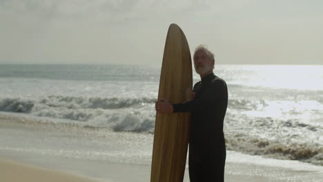 hombre mayor con tabla de surf de pie en la playa de arena y soñando