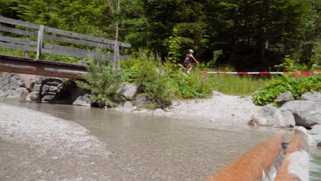 woman rides her mountain bike across a bridge over a stream on a sunny summer day