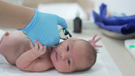 pediatrician's hand in a glove keeps a special device near infant's ear. care about baby health in the hospital.