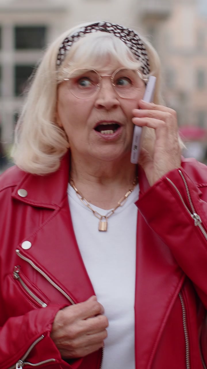Una donna anziana felice che ha una conversazione remota che parla su uno smartphone buone notizie pettegolezzi in una strada della città