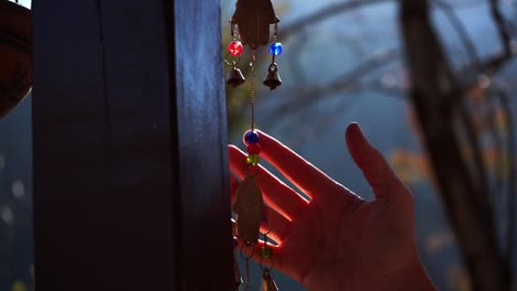 hand touching colorful metal wind chime hanging by a wooden column