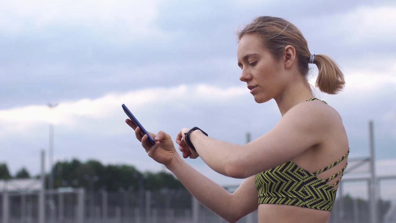 Giovane donna che controlla smartwatch e smartphone all'aperto