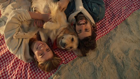 vista de arriba: pareja feliz en la playa sonriendo y mirando a la cámara. chico y chica con su perro posando y mirando a la cámara mientras se relajan en una playa soleada por la mañana