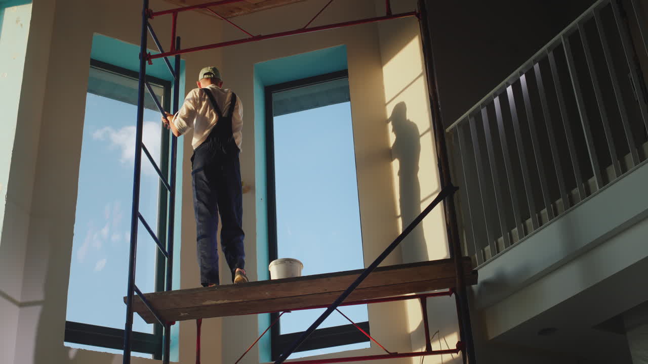 un constructor en mono prepara la pared de la casa. se encuentra en un andamio alto