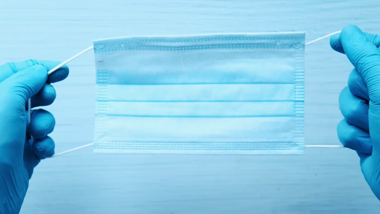 manos con guantes sosteniendo una máscara quirúrgica azul