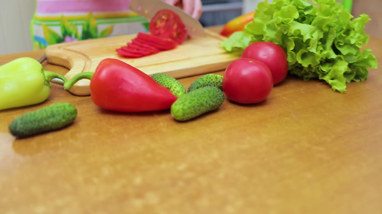Women's hands Housewives cut with a knife fresh tomato on the cutting Board of the kitchen table