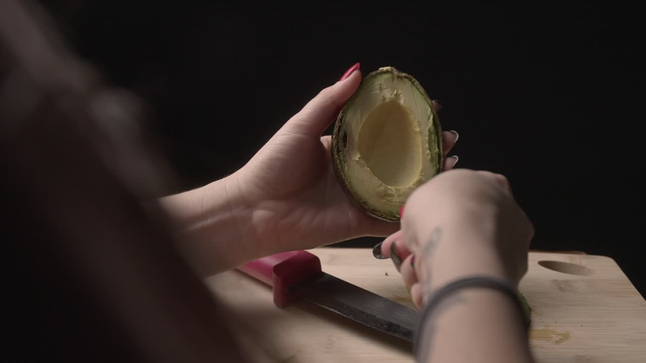 Close-up view of two women’s hands on a rustic wooden table as they peel a ripe avocado