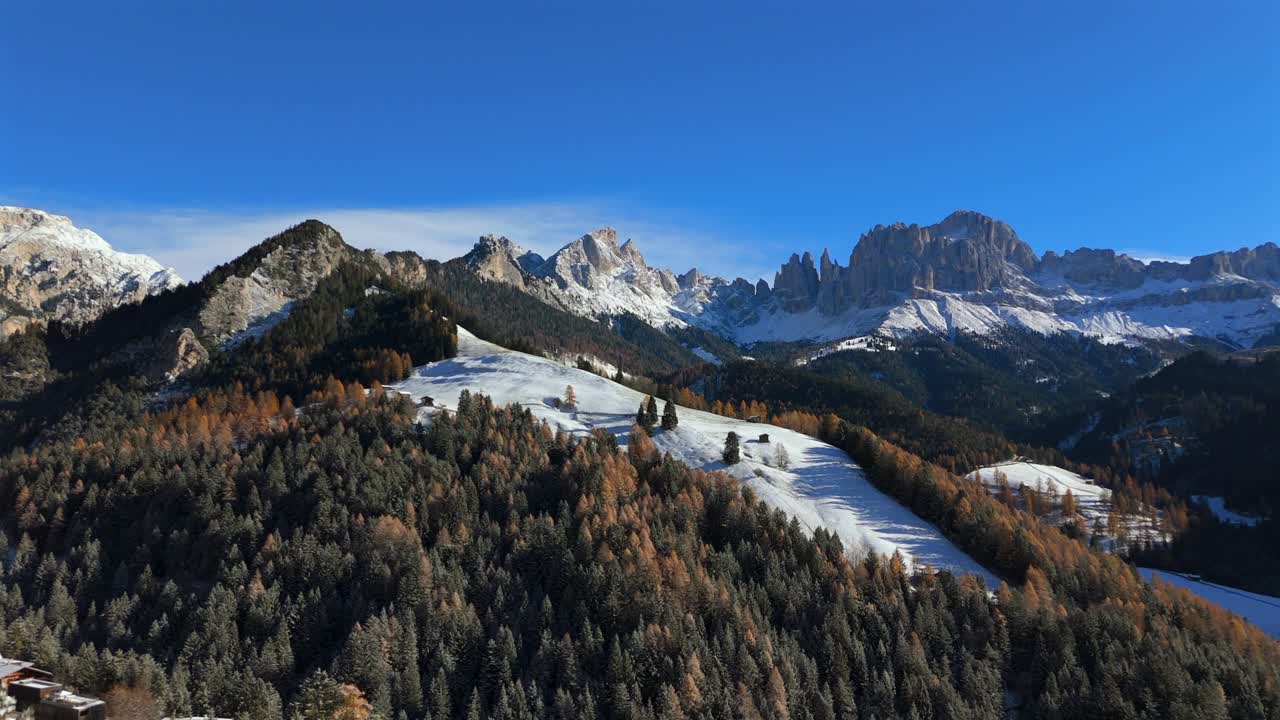 Stunning wide-angle view of the Rosengarten mountain range in the Dolomites, South Tyrol, with snow-covered hills, forest, wooden huts, and village rooftops in bright winter light