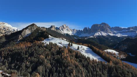 stunning wide-angle view of the rosengarten mountain range in the dolomites, south tyrol, with snow-covered hills, forest, wooden huts, and village rooftops in bright winter light