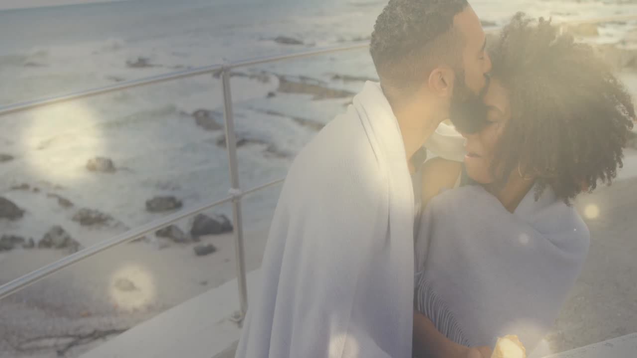 Sharing intimate moment, couple wrapped in blanket by ocean railing