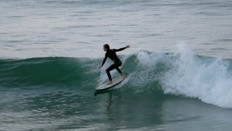 skillful fit caucasian man in wetsuit on surfboard paddles, surfs a wave and falls of his board into blue water of ocean