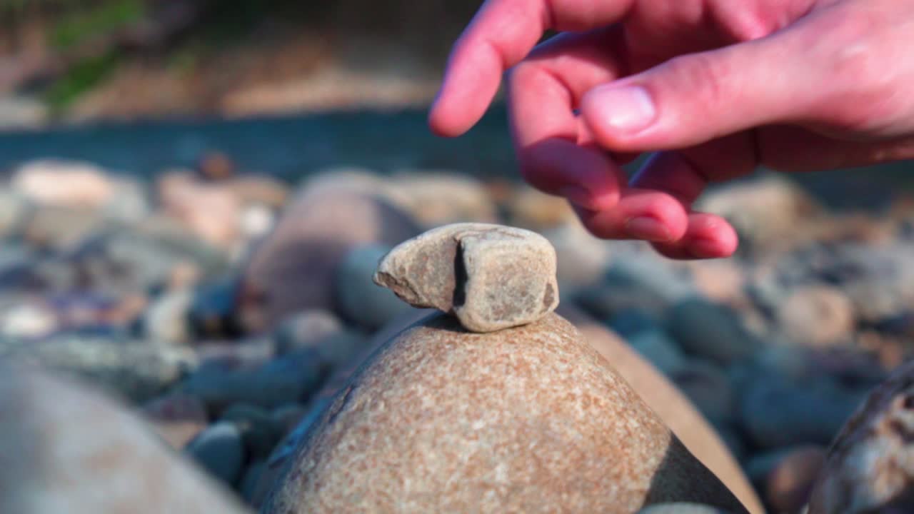 A hand pick up a small stone pebble on top of river bed rocks, low angle close up shot