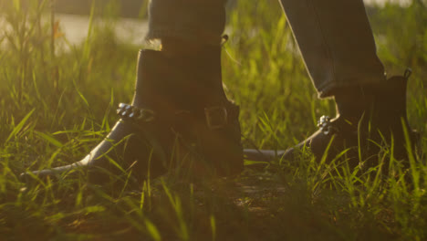 woman in boots walking through grass at sunset