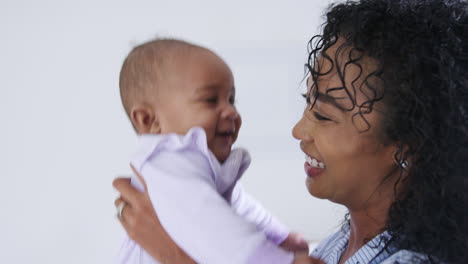 loving african american mother wearing pyjamas playing with baby daughter in bedroom at home