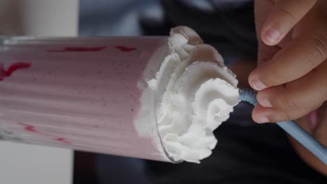 hand holding straw in pink milkshake with whipped cream