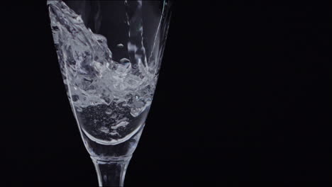 high framerate shot of water poured in a glass in front of a black background