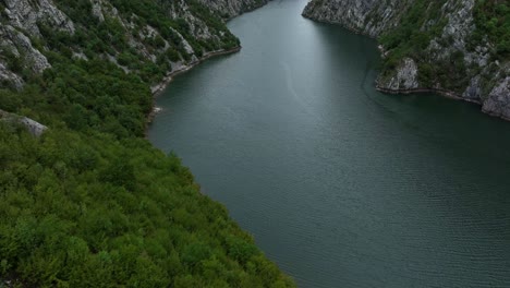 Aerial establishing tilt up of Lake Koman in Albania, with steep green cliffs surrounding the winding turquoise water