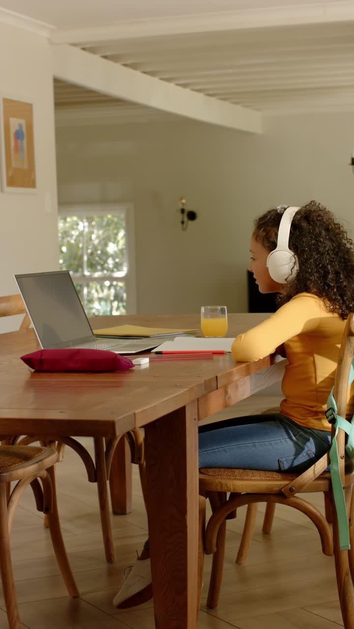Vertical video: Girl child in mustard-top joining class on laptop at table with headset, copy space