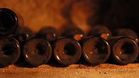 close-up view of dusty wine bottles arranged horizontally on a stone shelf in a dimly lit cellar.