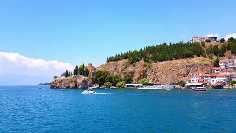 Beautiful-view-of-ancient-Ohrid-City-with-Church-of-Saint-John-the-Theologian,-Kaneo-and-buildings-on-harbor-from-boat-on-water-perspective