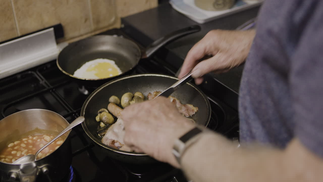 Man cooking breakfast with egg, bacon, beans, sausages and mushrooms on a stove