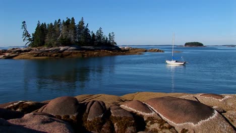 a sailboat is at anchor in a bay offshore a lobster village in stonington maine