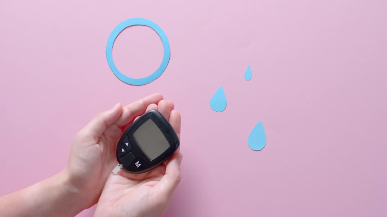 Hands of caucasian woman holding glucometer over blue drops and circle on pink, slow motion
