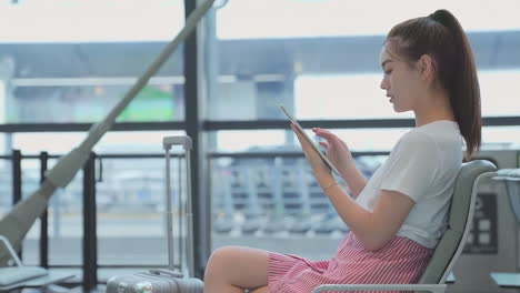 positive businesswoman with luggage sitting lounge play tablet computer while waiting for boarding