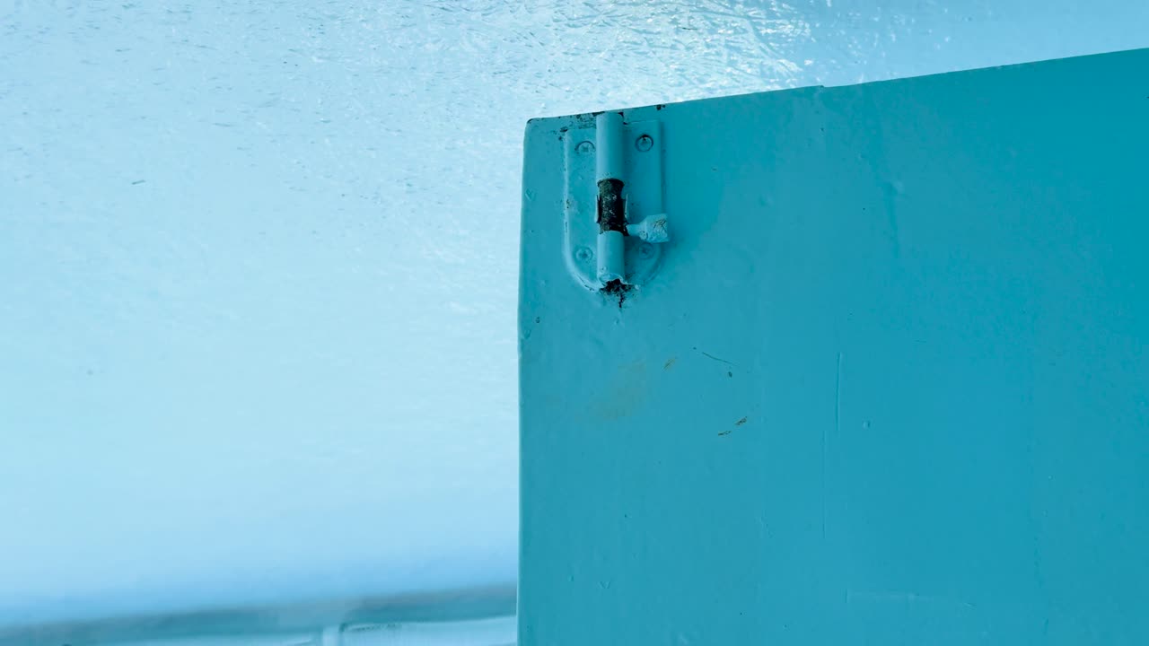 Close-up of a rusty metal hinge on a blue boat against the ocean backdrop in Phuket, Thailand. Bright, serene atmosphere