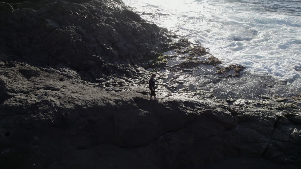ripresa aerea di una giovane donna che cammina lungo la costa e si possono vedere le onde del mare