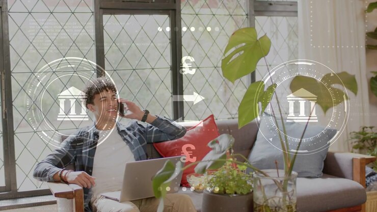 Uomo sul divano che risponde a una chiamata bancaria al telefono usando un laptop, con icone bancarie animate €¥£$ che si sovrappongono all'inquadratura.