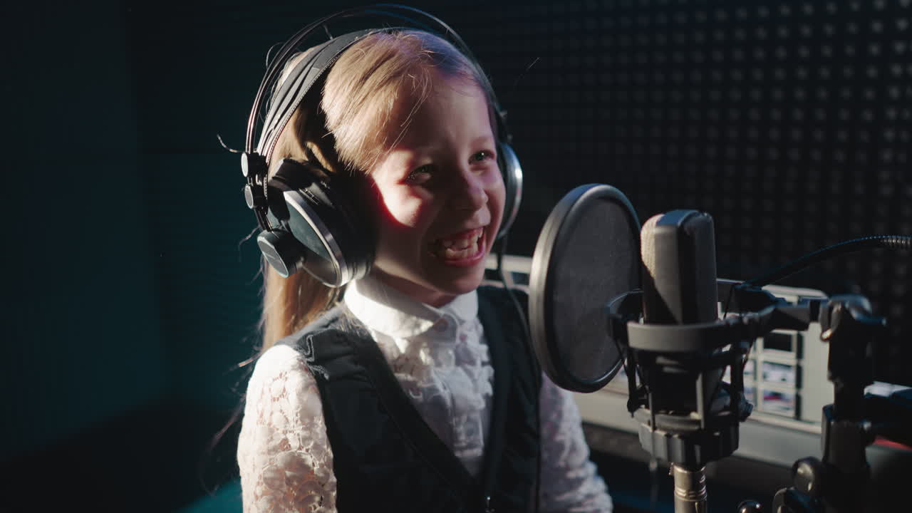 Giggling child in recording studio closeup. Joyful little girl enjoys getting ready for performing song using professional microphone. Soundproof room