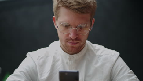 Retrato-De-Un-Usuario-Masculino-De-Un-Teléfono-Inteligente,-Un-Tipo-Guapo-Con-Camisa-Blanca-Está-Viendo-La-Pantalla-De-Un-Teléfono-Móvil-Moderno