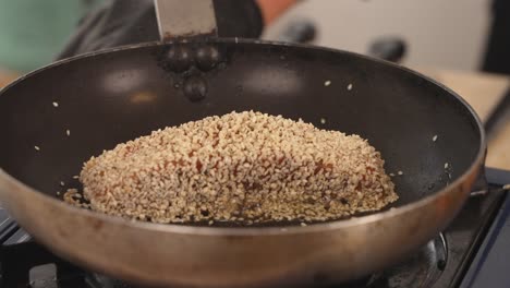 Delicious-fresh-salmon-fillet-cooking-on-shallow-frying-pan-with-oil-splattering-and-sesame-seeds-popping,-close-up-tataki-seafood-gourmet-shot