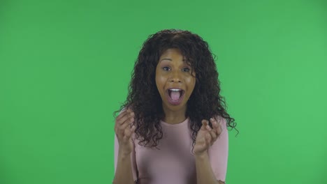 portrait of beautiful african american young woman is looking at camera with shocked and surprised wow face expression. burning brunette with wavy hair in jeans and a beige blouse on a green screen in the studio