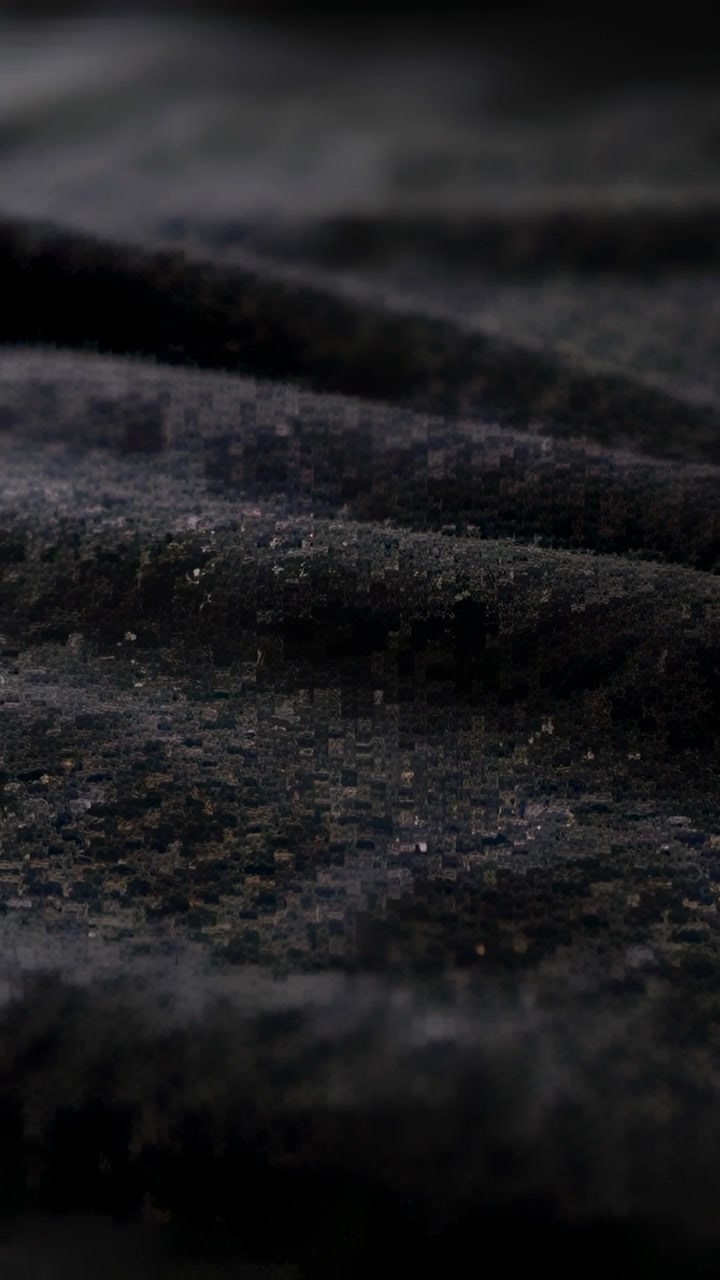 Vídeo vertical: Câmera deslizante capturando tecido de pelúcia preto em macro, revelando fibras e textura.