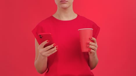 woman holding phone and cup in red shirt on red background