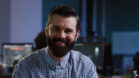 vista cercana del joven hombre de negocios barbudo sonriendo a la cámara en la oficina