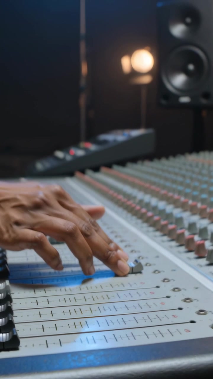 Vertical video: Sliding finger, dark-sleeved hands adjusting faders at studio desk, balancing mix