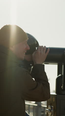 un padre sostiene a su hijo para mirar a través de un telescopio, el hijo mira a través de él mientras el padre sonríe, con la cálida luz del sol reflejándose en ellos