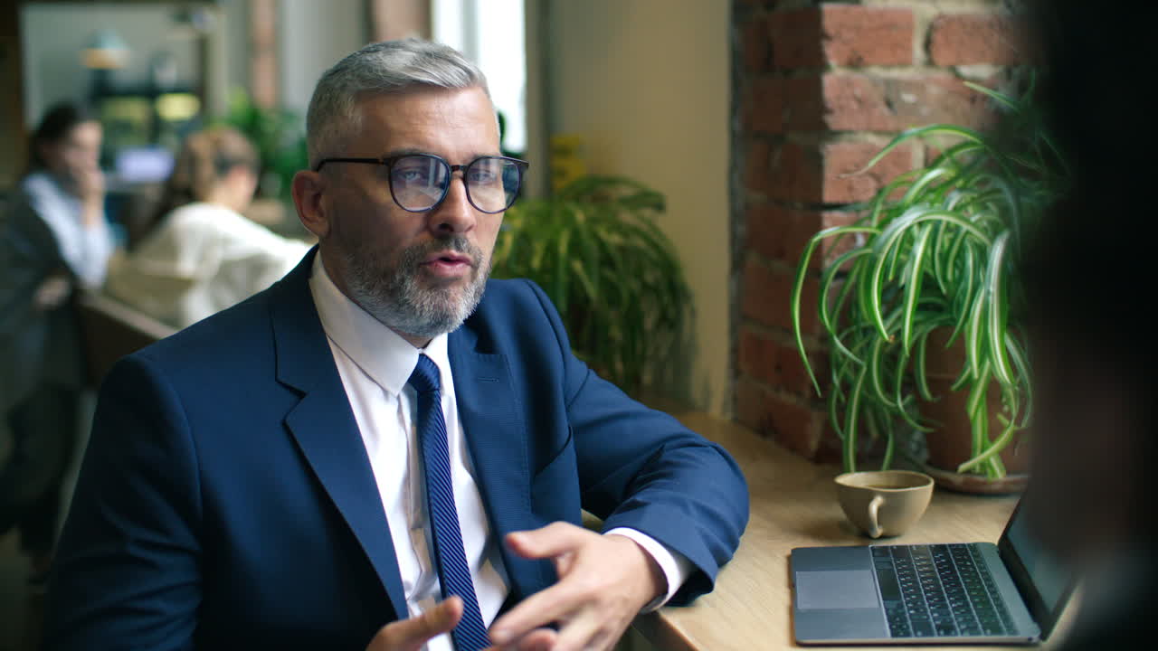 Mid-Aged Businessman Having Discussion with Colleague at Table in Cafe