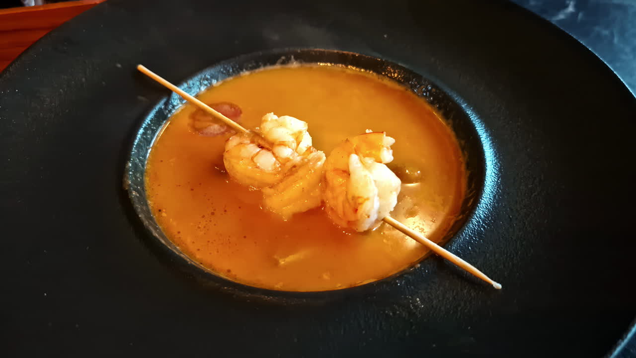Creamy orange soup with shrimp on skewers, served in a stylish black plate