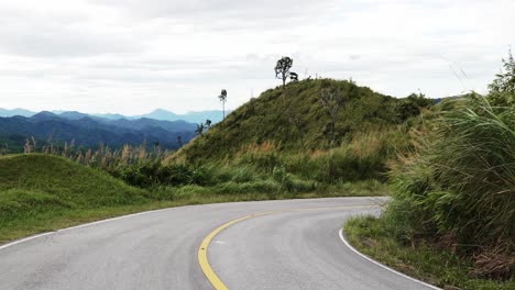 camino vacío con colinas de hierba ventosas onduladas en el costado, día nublado, montañas a distancia
